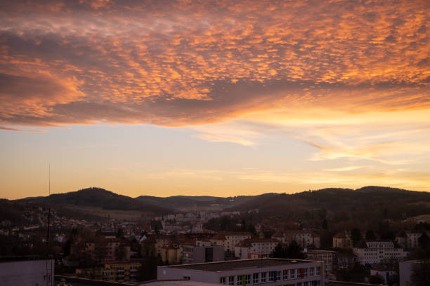 Captivating sunset with vivid orange and red hues, casting a warm glow over silhouetted hills and a tranquil townscape. Ideal for nature, evening, and landscape themes.