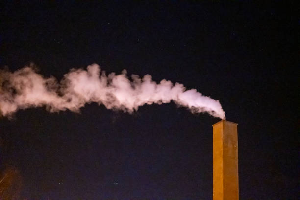 An industrial chimney emits a trail of smoke under a clear, star-dotted night sky