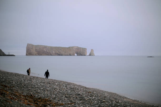 Shot of two distant persons walking along beach by famous Rocher Percer in Quebec. Taken in Quebec, Canada, during the day.