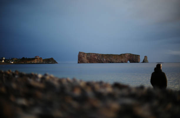 Shot of a middle aged man admiring the Famous Rocher Percer on a distant beach. Taken in Quebec, Canada, during the day.