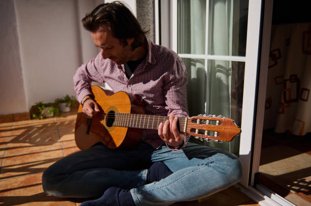 istock Man playing acoustic guitar while sitting on a sunny home patio 2196978338