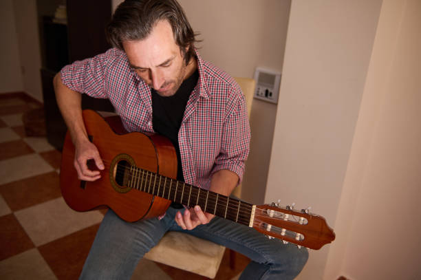 istock Man playing an acoustic guitar while seated in an indoor environment 2196978453