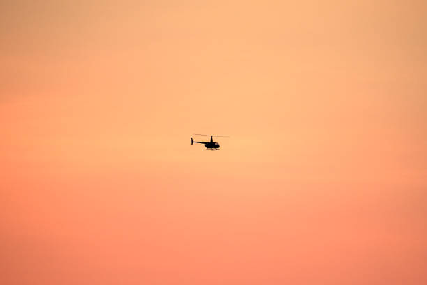 Silhouette of a helicopter flying against a vivid orange sky during sunset, creating a serene and atmospheric scene perfect for themes of exploration, travel, and freedom.