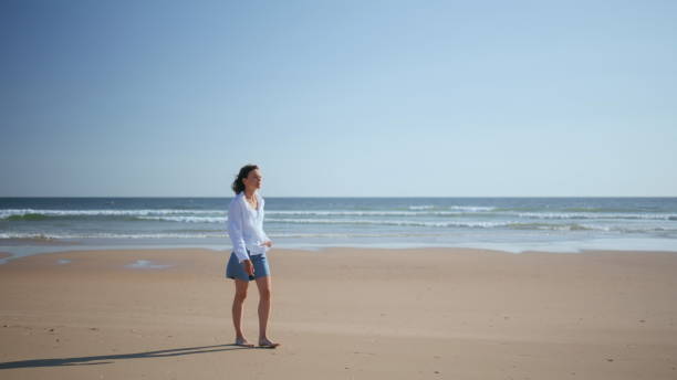 istock Brunette walking sandy shoreline in sunlight. Carefree woman exploring beach 2196983120