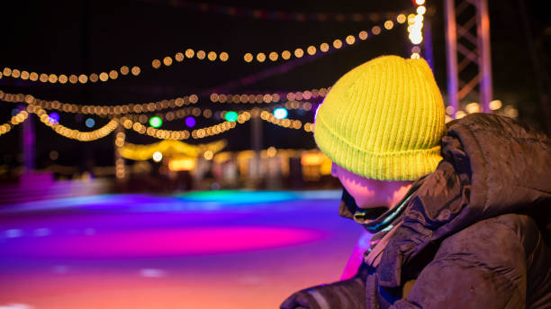 istock A boy looks at an ice rink illuminated with pink and blue lights. 2196986389