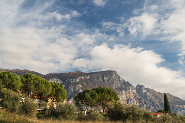 Mountain silhouette and evergreen trees against cloudy blue sky in Varenna, Lombardia, Italy