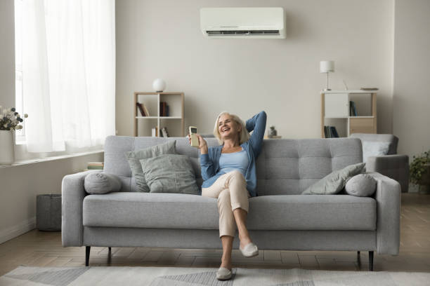Woman relaxing on sofa holding remote control managing temperature inside