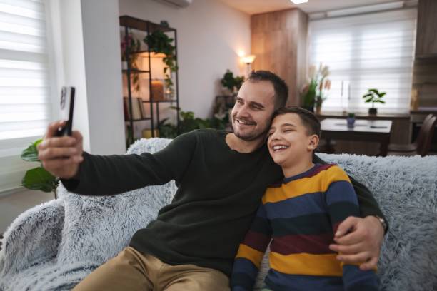 istock Father and son taking a selfie on the sofa, enjoying time together at home 2196993612