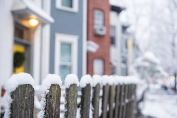 This is a photograph with selective focus of a wooden picket fence covered with snow on a winter morning in residential Brooklyn, NY.