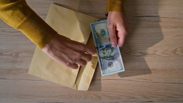 istock Hands placing dollars envelope on office desk closeup top view. Unknown woman 2196998794