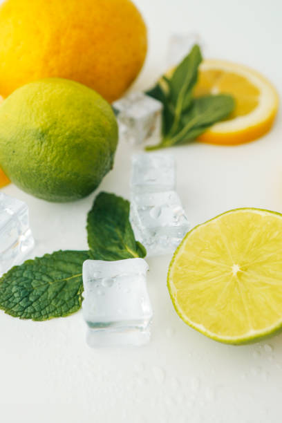 Fresh lime and lemon halves with mint leaves and ice cubes on a white background. A vibrant composition showcasing citrus fruits, perfect for healthy food, drinks, or summer themes