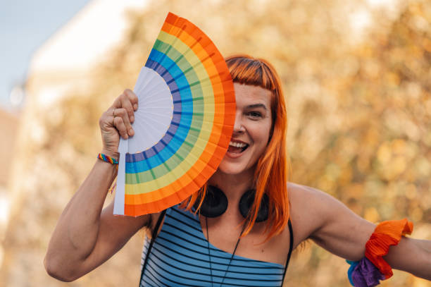 istock Happy activist hiding face with rainbow fan at lgbt parade 2197042394