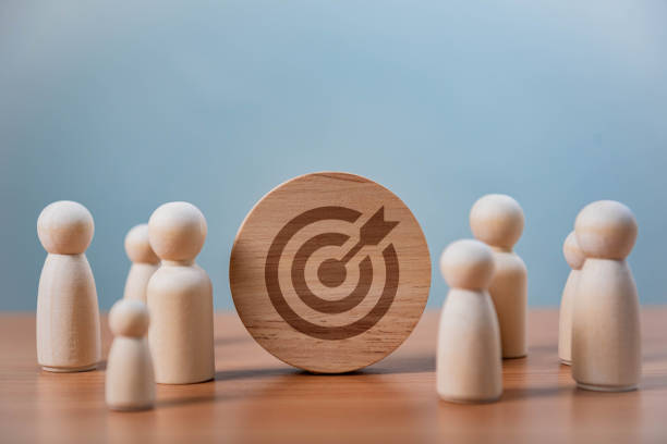 istock Teamwork and Business Goals Execution. A wooden disc with a bullseye and arrow icon is placed among wooden figures, symbolizing goal setting, business strategy, leadership, and teamwork. 2197044662