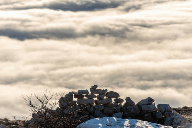 A scenic composition of a snow-covered stack of rocks on a mountaintop above a sea of clouds. The tranquil setting portrays natural serenity and an elevated perspective, evoking feelings of calmness and wonder. Ideal for concepts like peaceful landscapes, nature's beauty, and calm reflections.