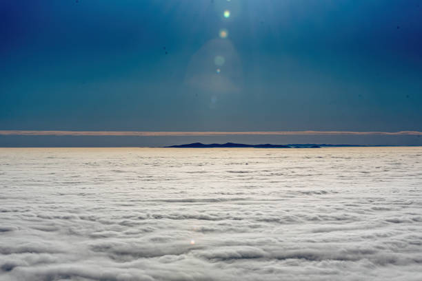 A serene view of mountain peaks emerging above an extensive layer of white clouds under a deep blue sky, capturing the essence of calm and stillness in nature.