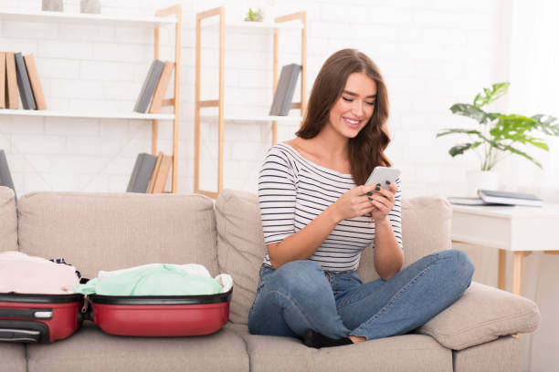 istock Young Woman Relaxing on a Sofa While Checking Her Phone Beside an Open Suitcase 2197047828