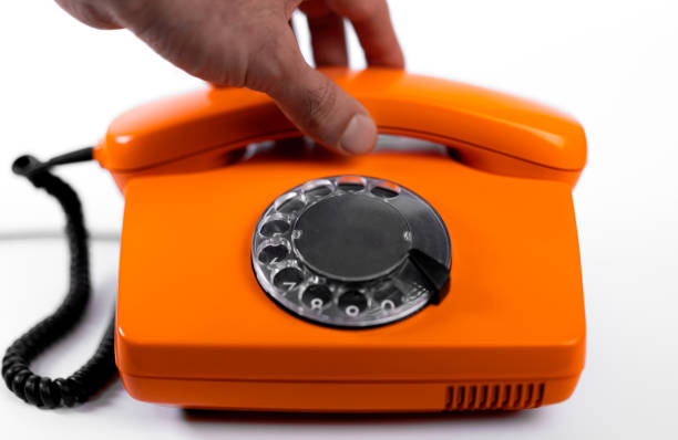 A hand approaches a bright orange rotary phone, preparing to lift the receiver. The retro phone contrasts with a clean, minimalistic background.