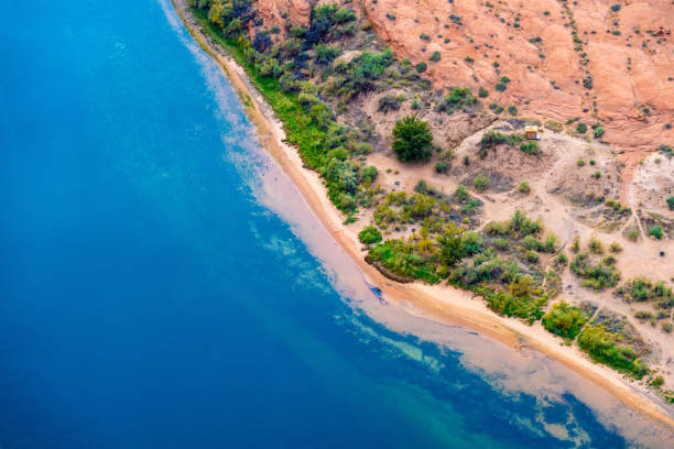 Stunning vibrant aerial view of the Colorado River winding through the Grand Canyon in Arizona, showcasing vibrant blue waters, lush green riverbanks, and rugged desert terrain. This breathtaking perspective highlights the beauty of nature’s contrast in the Southwest.