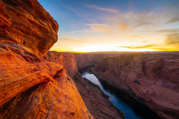 Sunset over the Grand Canyon and Colorado River in Arizona, where dramatic canyon walls glow in golden light. This stunning landscape captures the beauty of the Southwest’s rugged terrain, deep gorges, and winding river, creating a mesmerizing natural wonder.