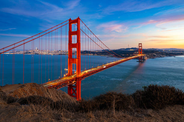 Experience the breathtaking sunset over the Golden Gate Bridge in San Francisco, California, with city lights reflecting on the bay. This iconic landmark offers a stunning view of the illuminated suspension bridge, vibrant sky, and scenic waterfront.