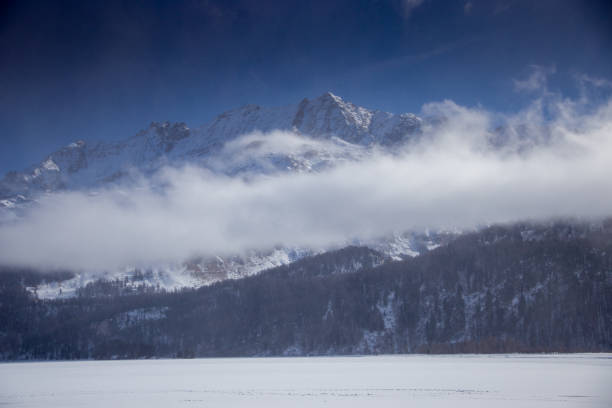 Frozen lake covered in snow surrounded by dramatic alpine peaks