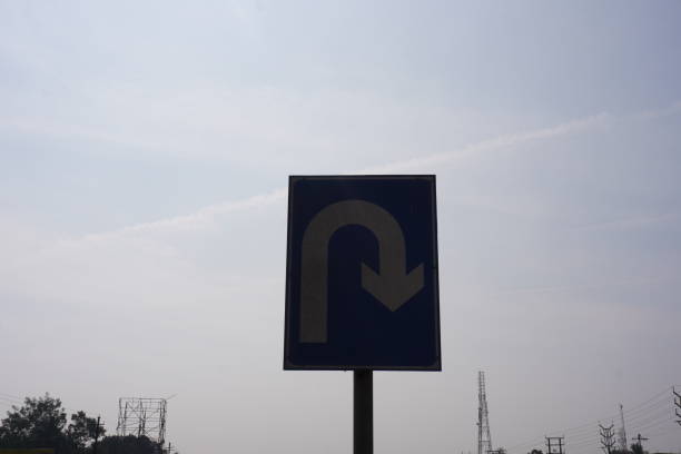 The u turn sign board has put beside the highway with clear blue sky background