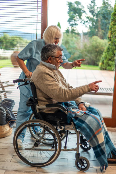 istock Nurse assisting elderly man in wheelchair pointing at something 2197056554
