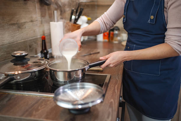 Chef pouring milk into saucepan while cooking on stove