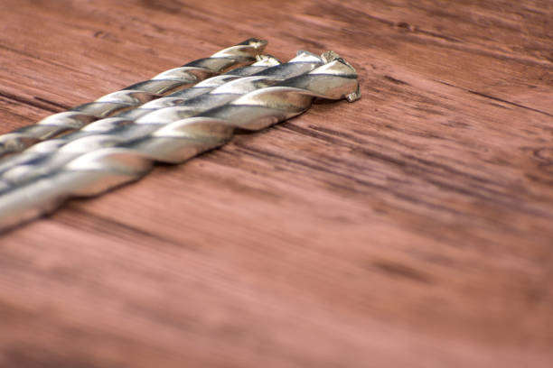 Drill bits neatly arranged on a wooden surface. Metallic finish of bits contrasts with natural wood grain, highlighting their sharpness and precision. Concept of craftsmanship and attention to detail