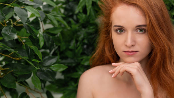 Young tender redhead young girl with healthy freckled skin looking at camera with pensive expression, nature background, panorama with free space