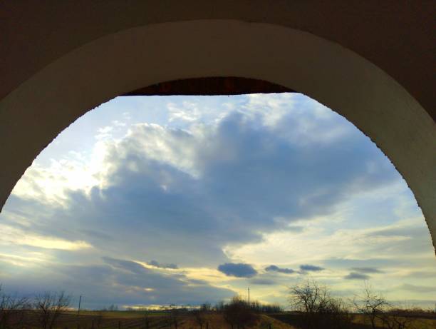 Arch in the wall through which a blue cloudy beautiful sky is visible. Architecture and nature.