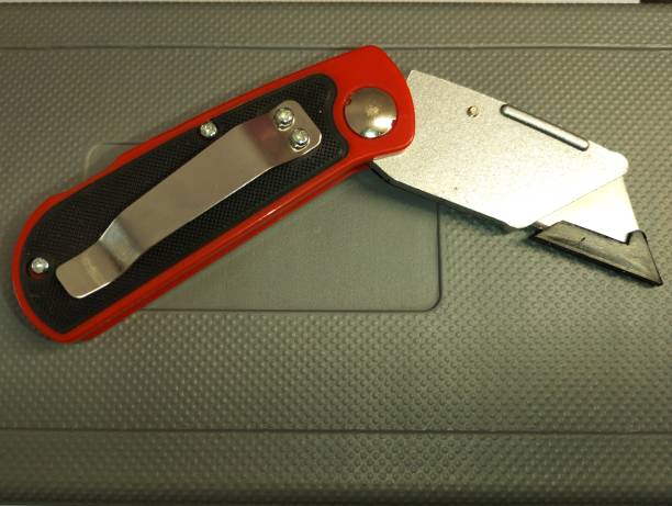 A folded red utility knife lies on a gray background. A construction tool for cutting.