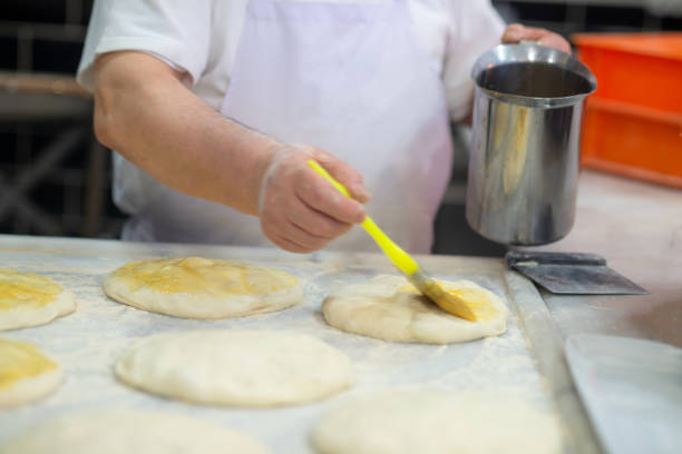 Old master baker brushes eggwash onto traditional Turkish pita breads called 'trnak pide' on marble countertop in front of wood fired oven at a kebab restaurant in Istanbul, Turkey