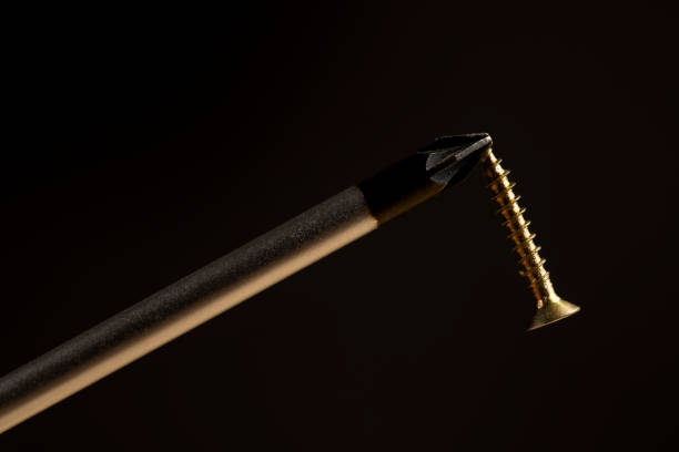 screwdriver with a magnetic tip and golden decorative self  tapping screws for fixing wood, new golden yellow  screws  on a black background