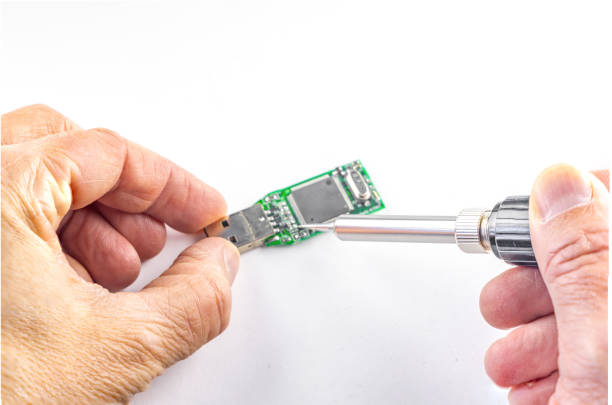 Soldering iron in the hands of a man who repairs a damaged flash drive, on a white background
