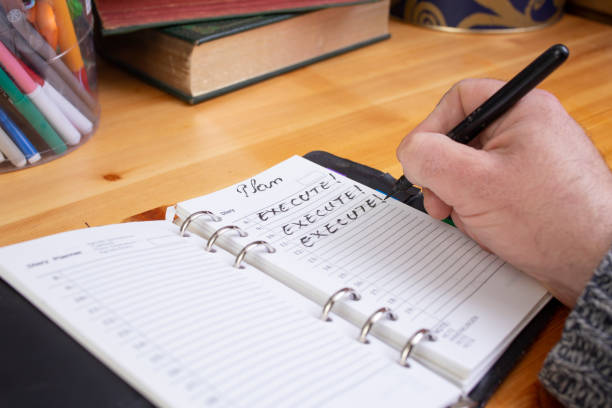 istock Male hand writing Execute! word on a note book diary, working with a business plan concept, wooden desk background 2197079460
