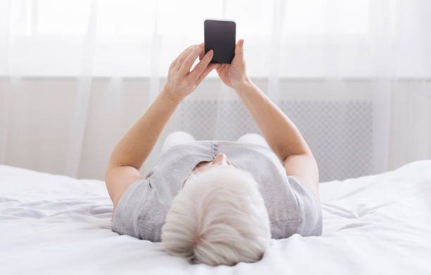 Senior woman surfing phone while lying in bed
