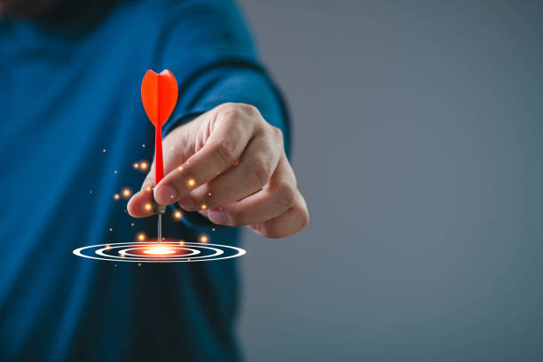 istock Hand aiming a dart at a glowing target, symbolizing focus, precision, and success in achieving goals 2197083368
