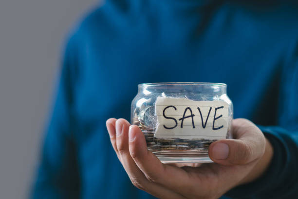 istock Person holding a glass jar with a 'SAVE' label and money inside, emphasizing the concept of saving and financial management. 2197083382