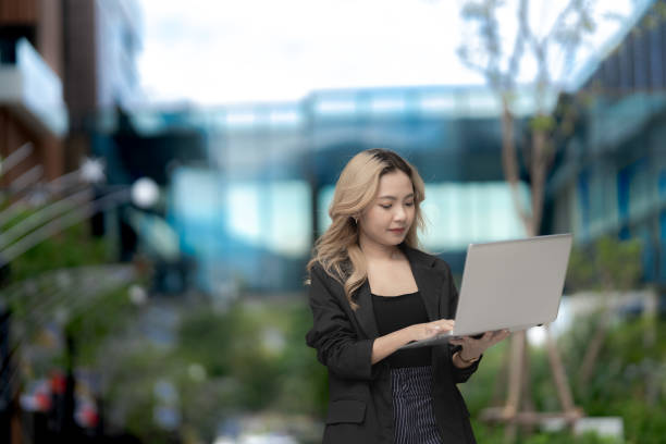 istock Confident businesswoman walking outdoors with a laptop, showcasing modern technology and professional ambition. A blend of urban greenery and innovation for a dynamic lifestyle. 2197085647