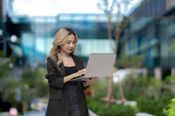 istock Confident businesswoman walking outdoors with a laptop, showcasing modern technology and professional ambition. A blend of urban greenery and innovation for a dynamic lifestyle. 2197085697