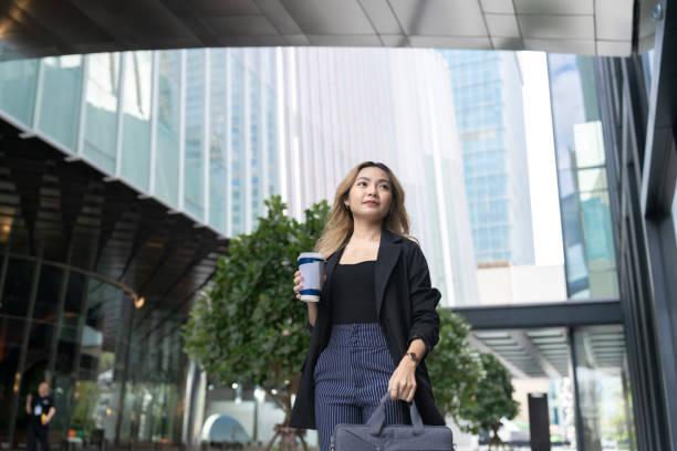istock A confident young professional woman walking outdoors in a modern urban setting, holding a coffee cup, surrounded by greenery and glass buildings, exuding elegance and contemporary style. 2197087806
