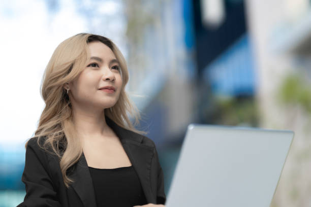 istock Smiling professional woman working on a laptop outdoors in a modern urban setting. A positive and inspiring image for themes of technology, career growth, and success. 2197088082