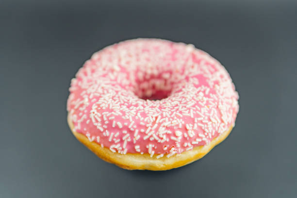 istock Image of a single pink glazed doughnut with pink sugar sprinkles, placed on a neutral surface against a light background Simplistic food photography style, suitable for a culinary blog or advertisem 2197088162