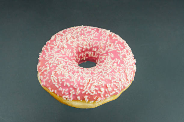 istock A single, vibrant pink frosted doughnut with sprinkles sits centrally on a light grey surface Realistic high-angle image 2197088177