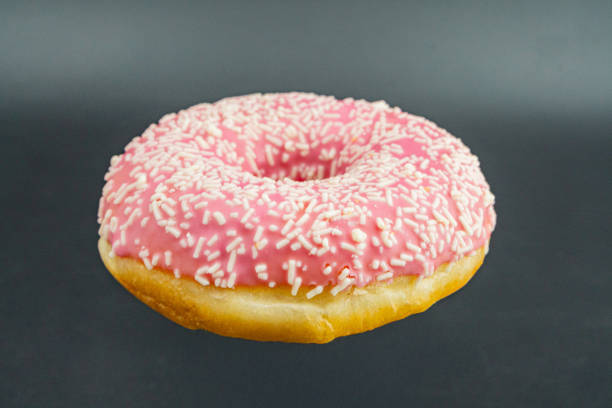 istock A single, vibrant pink glazed doughnut with textured glaze and contrasting sugar sprinkles, golden brown base, centered against a dark background 2197088184