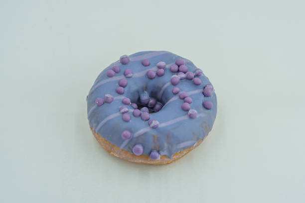 istock Image of a single, purple-glazed doughnut with white sprinkles on a neutral-toned surface 2197088191