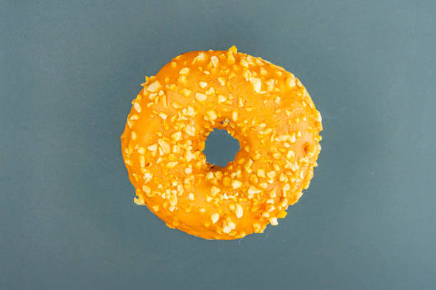 istock Image features a center-framed circular doughnut, orange glazed and topped with sprinkles, possibly nuts or seeds Background is neutral, likely used for culinary presentation or advertising 2197088194