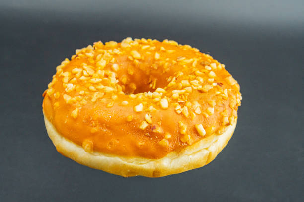 Golden-brown glazed doughnut with textured crushed nuts on a light gray background