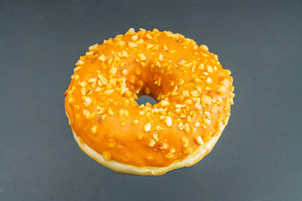 istock A centered, golden-brown doughnut on a light surface, with orangey-yellow icing and textured nutseed topping, photographed in a straightforward style for food context 2197088221